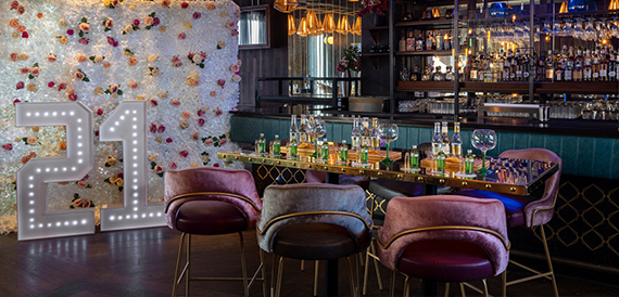 Bar area with a flower wall, light-up number decoration and pink velvet chairs