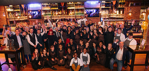 Large group of staff members celebrating together in front of the bar