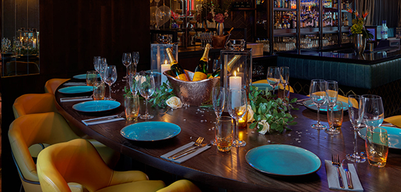 Dining table set with turquoise plates, candles and a champagne bucket beside the bar
