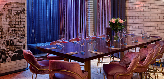 Private dining table with pink chairs, roses and glassware beside patterned curtains