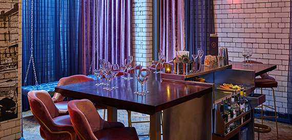 Bar area with velvet chairs, glassware and a drinks trolley beside brick walls