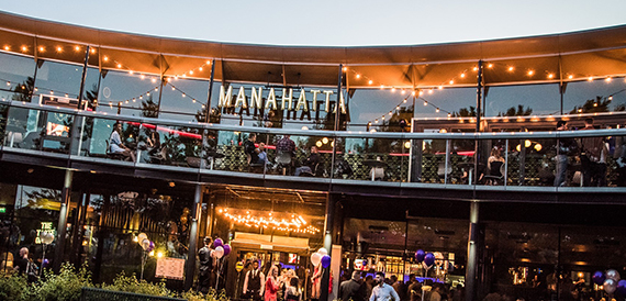 Exterior of the Manahatta building lit up at dusk with guests on the terrace