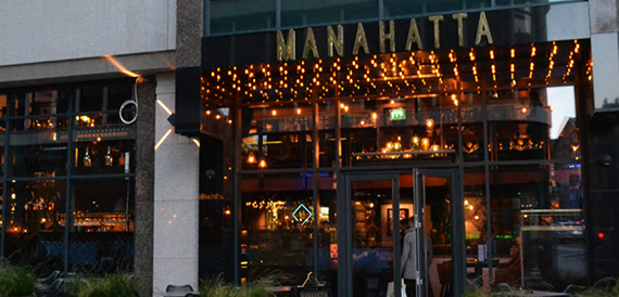 Exterior entrance of Manahatta lit up at dusk with festoon lighting along the canopy