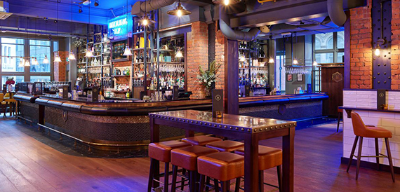 Bar area with exposed brick pillars, a high table and shelves of spirits behind the counter