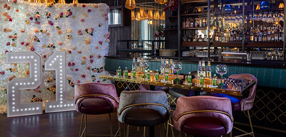 Bar area with a flower wall, light-up number decoration and pink velvet chairs