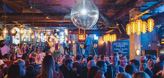 Crowded bar beneath a large disco ball and rows of gold lantern lights