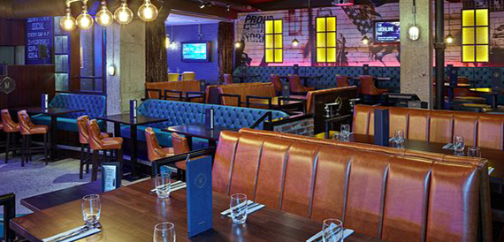 Dining booths in tan leather and teal upholstery lit by yellow-lit windows