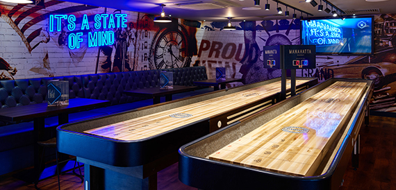Shuffleboard tables lit beneath a neon sign reading it's a state of mind