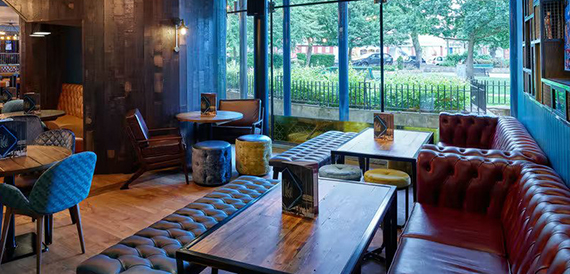 Lounge seating with a red leather sofa and mismatched stools beside park-facing windows