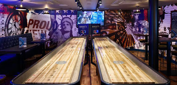 Twin wooden shuffleboard tables beneath an American-themed wall mural