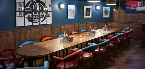 Long private dining table with red and teal chairs beneath framed boxing artwork