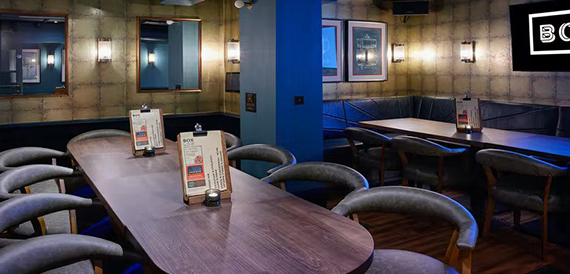 Private dining tables with grey chairs set beneath a neon sign reading box