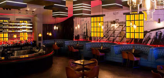 Curved bar with amber-lit window panels and booth seating beside a mural
