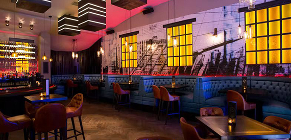 Booth seating lit by amber window panels beneath a city skyline mural