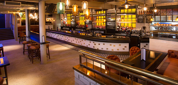 Curved bar counter with illuminated shelving beneath a mezzanine seating area