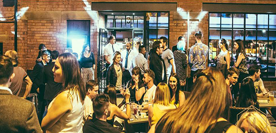 Crowd of guests socialising on an outdoor terrace at night beside a brick building