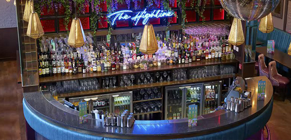 Teal bar counter beneath a neon Highline sign and gold pendant lights