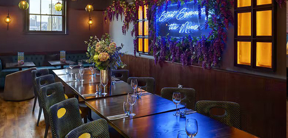 Private dining table with green chairs and flowers beneath a neon sign amid trailing wisteria