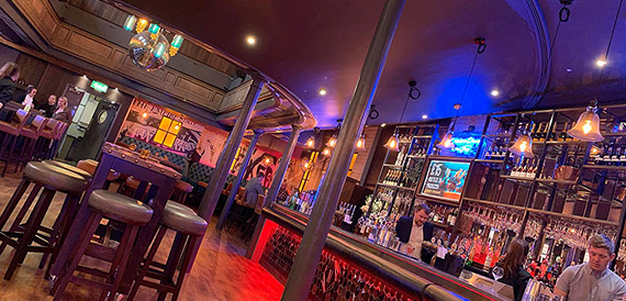 Curved bar counter with staff serving drinks in front of illuminated shelving
