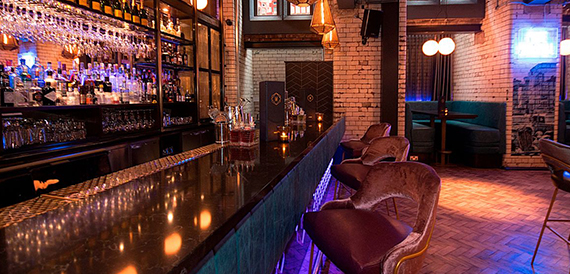 Bar counter with hanging glassware beside teal booth seating and exposed brick walls