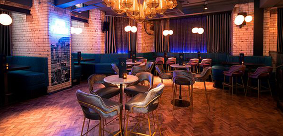 Lounge seating beneath a large gold chandelier with teal booths and brick walls
