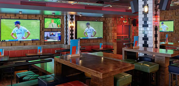 Sports bar with screens showing cricket beside orange booth seating