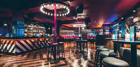 Dark bar with a glowing pink circular light fixture and high stools