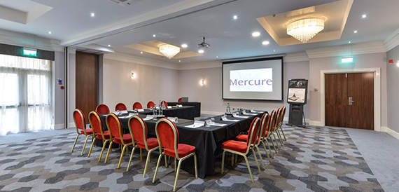 Meeting room set u-shape with red chairs facing a screen showing the Mercure logo.