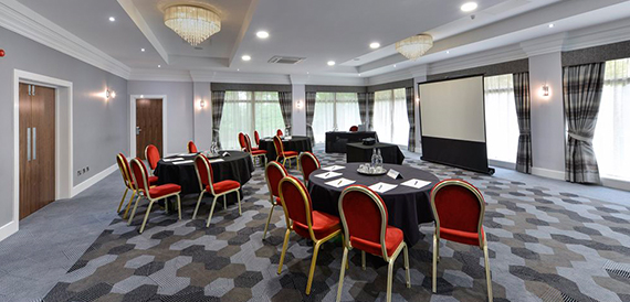 Meeting room set with round tables, red chairs and a projector screen.