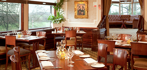 Restaurant with dark wood tables, leather chairs and a framed painting on the wall.