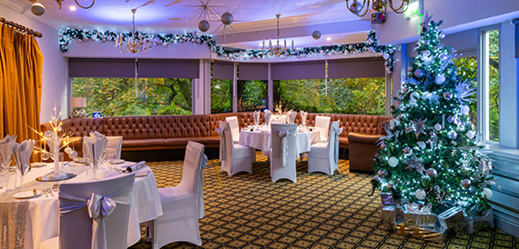 Dining room decorated for Christmas with a lit tree, garlands and leather sofas.