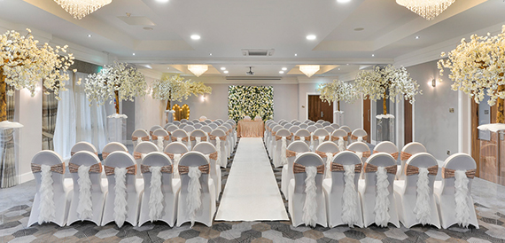 Wedding ceremony aisle lined with white chair covers and blossom tree displays.