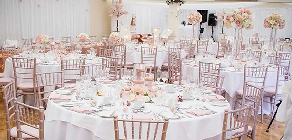 Wedding reception room with round tables, blush chiavari chairs and pink floral displays.