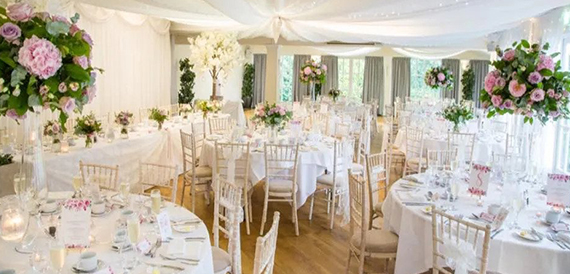 Wedding breakfast marquee with round tables, pink floral centrepieces and gold chiavari chairs.