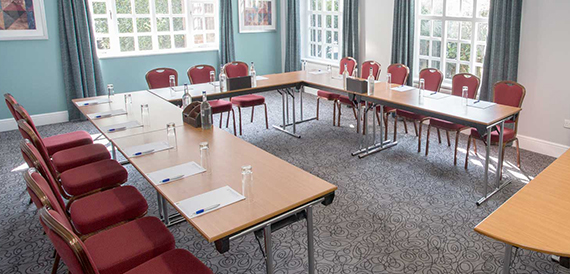 Meeting room set u-shape with red chairs and tall leaded windows.