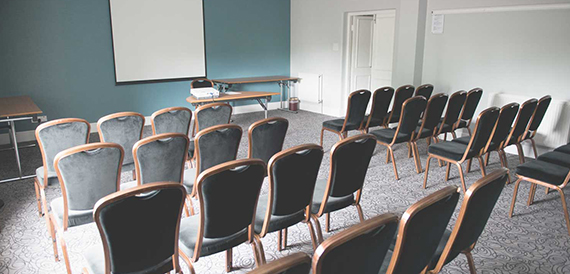 Meeting room set theatre-style with rows of grey chairs facing a projection screen.