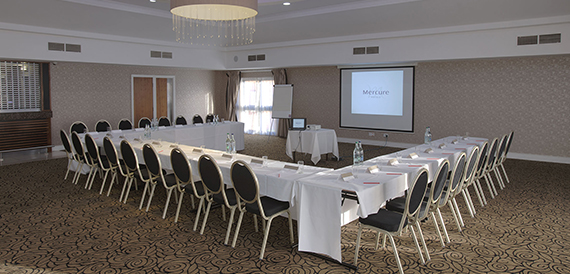 Meeting room with tables arranged in a u-shape facing a projector screen.