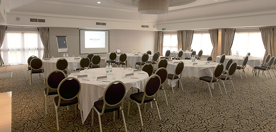 Conference room set cabaret-style with black chairs facing a projector screen.