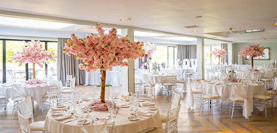 Wedding reception room with round tables, blossom tree centrepieces and chiavari chairs.