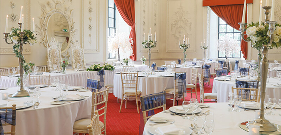 Banqueting hall set for a wedding with round tables, tall candelabras and an ornate mirror