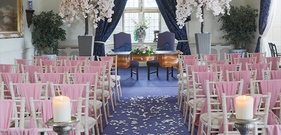 Wedding ceremony room with pink chair sashes, blossom trees and blue curtains