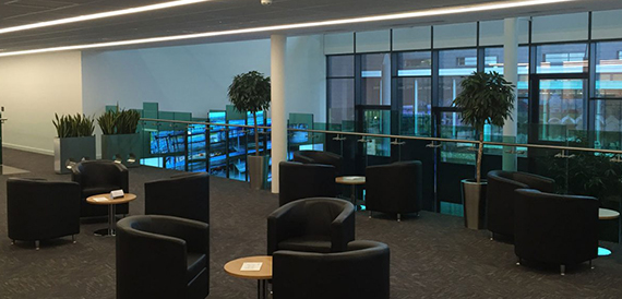 Breakout mezzanine with black tub chairs, small tables and a glass balustrade.