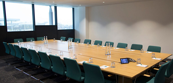 Boardroom with a long table, teal chairs and a city view through the windows.