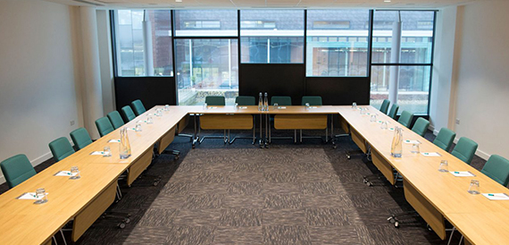Boardroom set u-shape with green chairs facing tall windows.