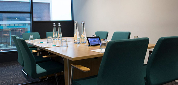 Meeting room with a wooden table, green chairs and water bottles set out.