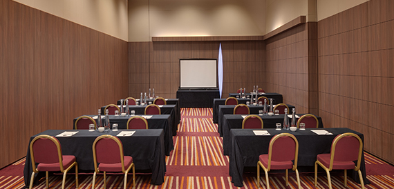 Meeting room set cabaret-style with dark-clothed tables and a projector screen