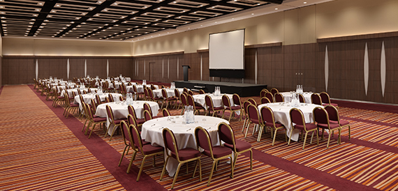 Ballroom set banquet-style with round tables facing a large projector screen