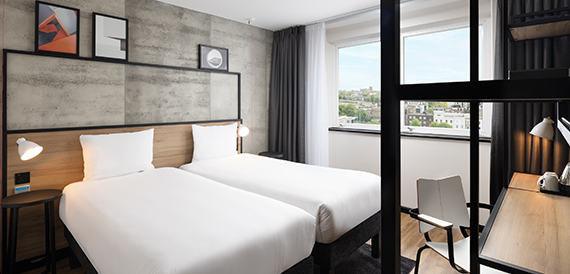 Twin hotel room with two single beds beside a glass-partitioned desk area