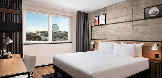 Hotel bedroom with a double bed, wood-panelled headboard and a city view