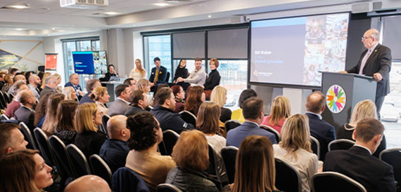 Conference audience seated facing a speaker at a podium and panel on stage